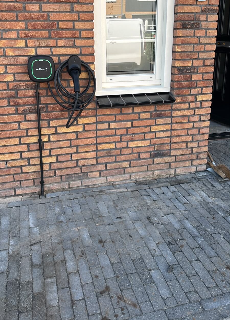 Oplaadpunt aan een gevel, gezien vanaf een geplaveide oprit