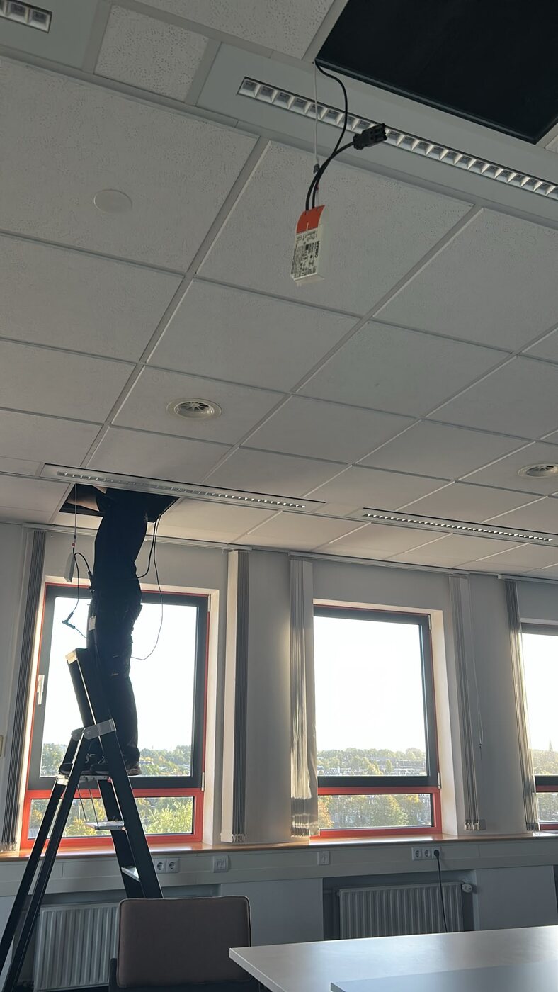 Installateur werkt via een ladder boven een systeemplafond
